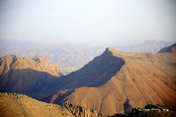 Fototapeta na wymiar High imposing mountains overlooking the village buildings, Jabal Akhdar, towards Nizwa, Oman