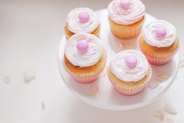 Vanilla cupcakes with white icing and candy topping served on cake stand with pink rose petals sprinkled for decoration