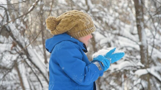 Child blow on fresh snow lying in his hands. Little boy having fun playing with fresh snow. Active outdoors leisure for kids in snowy winter day.