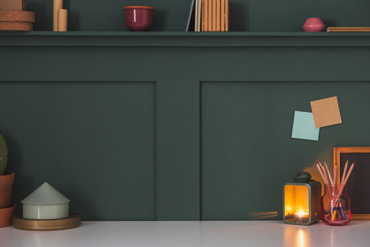 Home workspace, creative desk with wooden supplies, tealight lantern burning and dark wall.