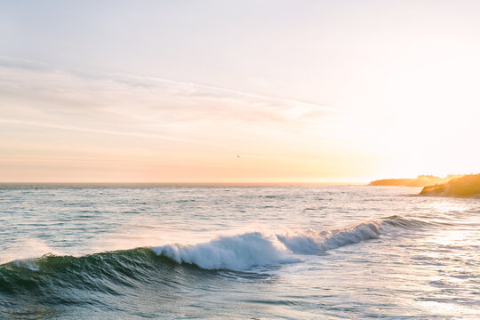 Golden hour sunset with Pacific ocean waves crashing along cliff shoreline of Santa Cruz Bay on California coast