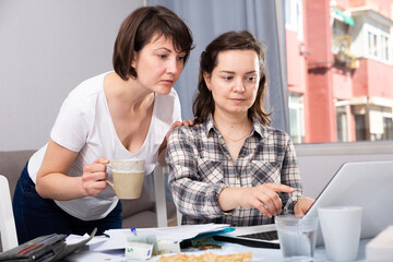 Obraz premium Two smiling women sitting at home table with laptop. High quality photo