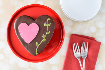 Heart shaped chocolate cake on a red platter and gold background, Valentine’s day treat
