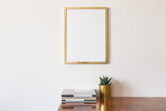 Frame on the wall and desk with plant and books. Stylish room interior. 