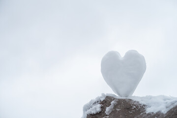 Fototapeta premium Heart shaped snowball standing on a stone with a snowy background