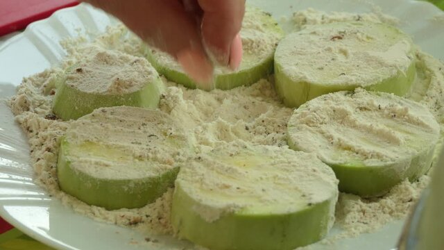 Organic food, eco food, vegetarian. The cook rolls slices of sliced zucchini in flour with spices near the hot stove before frying. Close-up shooting.