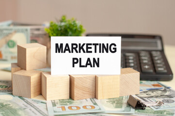 Paper card with text MARKETING PLAN. Calculator, flowers and brown background