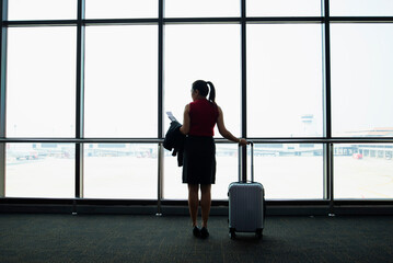 Image of woman in airport looking at taking off airplane, business