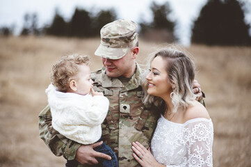 Young family portrait - a soldier father holding his son and a beautiful young wife