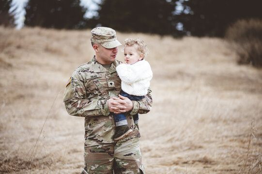 Portrait of a soldier father holding his son in a field