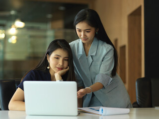 Two businesswomen working with paperwork and laptop in meeting room