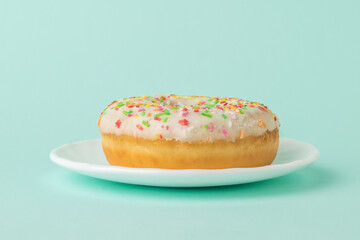 Fresh decorated donut on a white plate on a blue background.
