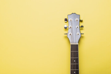 The neck of a classic six-string guitar on a yellow background.