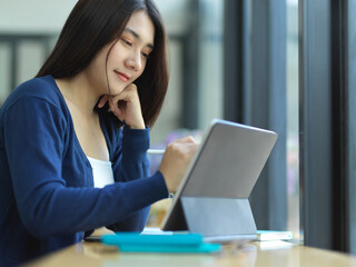 Female student doing assignment with digital tablet and stationery in cafe