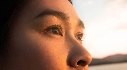Side view of happy hopeful woman looking away to nature reflection on water at sunset lakeside. Close up of her eyes.