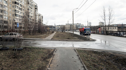 A sand lorry driving down the road. Mud and puddles on the roads, unmaintained lawns.
