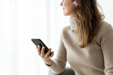 Naklejka premium Woman wearing wireless earbuds and using a mobile phone