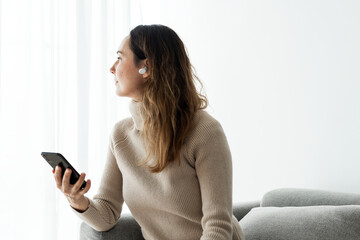 Naklejka premium Woman wearing wireless earbuds and using a mobile phone