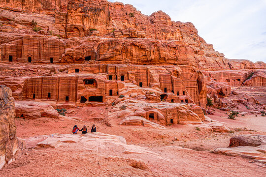 Jordan , Petra, Street of Facades, Tombs carved out of the pink Sandstone rock. Local people sitting in front of the tombs.