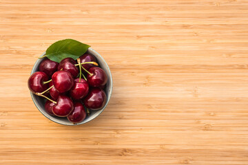 closeup of ripe dark red cherries in porcelain bowl on wooden chopping board with copy space on right