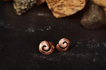 Handmade copper earrings in the shape of a shell on a black textured background. Jewelry product. Special gifts       