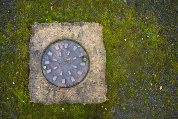 Storm drain access cover in mossy asphalt driveway, as a background
