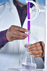 A scientist performs a titration in the chemistry lab, carefully adding a solution to a test tube, observing the reaction to determine concentration and analyze results.