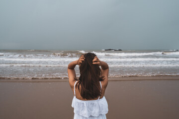 Fototapeta na wymiar Young woman feeling lonely and sad looking at the sea on a gloomy day