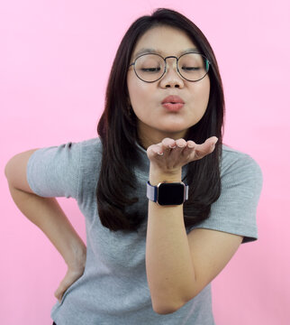Blowing kiss, Beautiful Asian (Indonesian) woman wearing a gray turtle neck shirt isolated on pink background