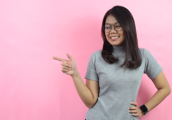 Pointing a side and smiling, Beautiful Asian (Indonesian) woman wearing a gray turtle neck shirt isolated on pink background