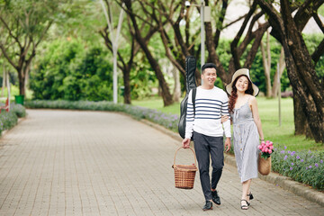 Obraz premium Happy young Asian couple with picnic baskets and guitar walking in city park