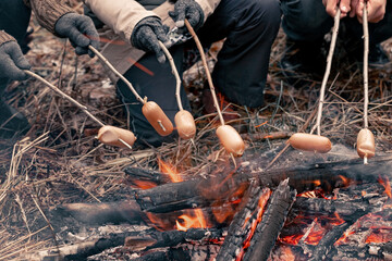 Fototapeta premium People frying barbecue sausages on the fire. Bonfire in the autumn forest. Campfire travel trip food
