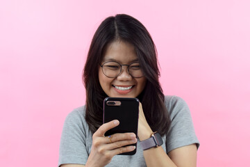 Happy with smartphone, Beautiful Asian (Indonesian) woman wearing a gray turtle neck shirt isolated on pink background