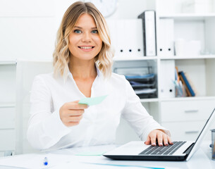Smiling girl in white shirt sitting at office desk in well-lit office. High quality photo