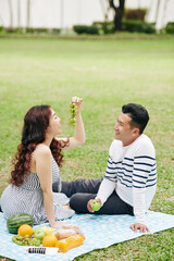 Young Asian couple eating fresh fruits when having romantic picnic in city park