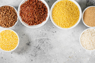 White and red rice, buckwheat, amaranth seeds, corn groats, quinoa and millet in white bowls on the...