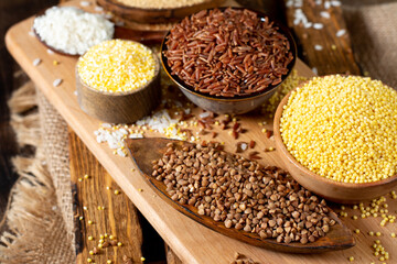 White and red rice, buckwheat, amaranth seeds, corn groats, quinoa and millet in bowls on a brown wooden table. Gluten-free cereals. Closeup