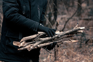 Male hands in black gloves collect firewood for the fire. Bonfire in the autumn forest. Campfire...