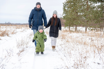 Cheerful child runs in the winter in the snow ahead, and his parents follow him. The family walks in winter.