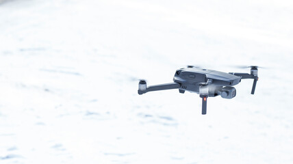 Naklejka na ściany i meble An unmanned quadcopter with a digital camera flies over the city in winter. The camera flies and takes pictures of the forest, the city. Close-up, blurred background. Modern technology, video filming 