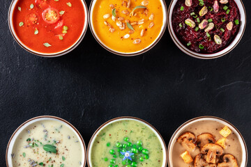 Vegan soup background with various cream soups and copy space, overhead flat lay shot on a black background
