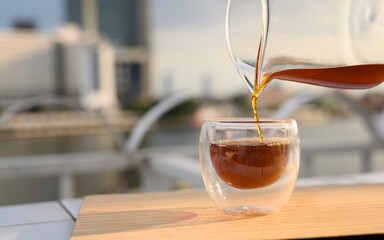 Close up pouring hot black coffee from the coffee pot into a cup on the balcony by the river. Copy space.