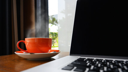Cup of hot cappuccino coffee with modern laptop on wooden table within cafe, Selective focus on coffee cup. Business workspace, modern lifestyle concept.