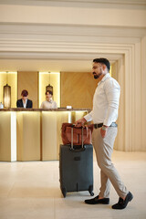 Confident successful elegant man with suitcase and briefcase standing in hotel lobby