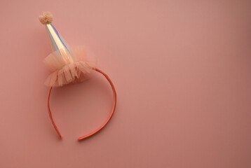 A pink hair band with a mother-of-pearl cap with a pompom rests on a pink background