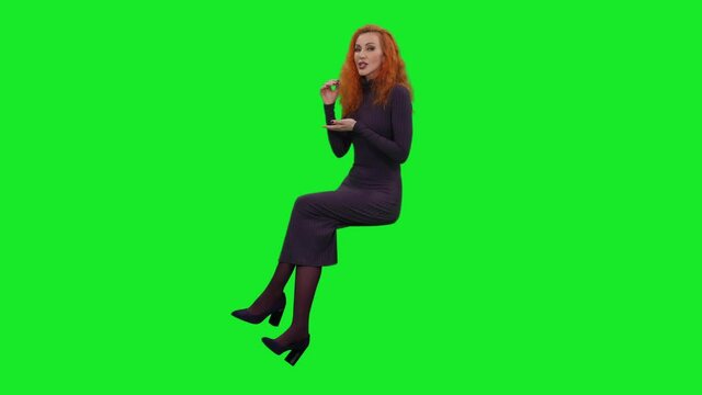 Elegant woman in dress sitting while telling the story and gesturing on green screen background, chroma key 4k pre-keyed footage