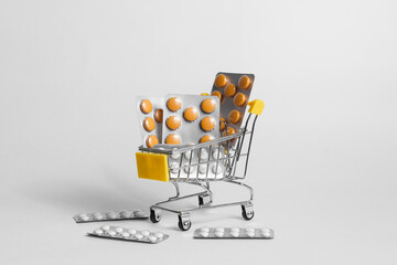 Miniature shopping cart with pile of assorted pills and medicines in blisters on white background in studio 
