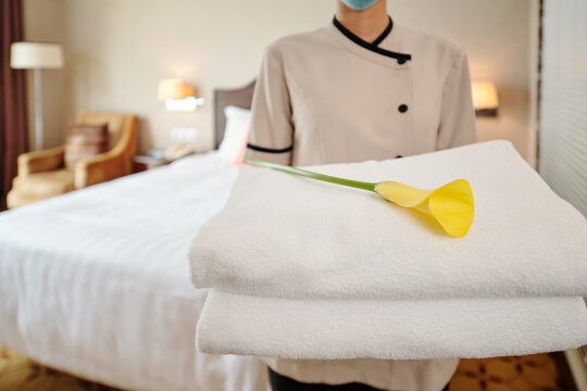 Cropped image of young female hotel maid standing in suite with stack of fresh towels and calla lily
