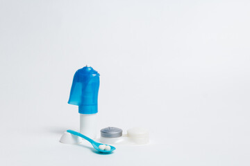 Eye drops and pile of pills in spoon placed on white background with container for contact lenses 