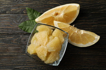Bowl with pomelo fruit slices and leaves on wooden background